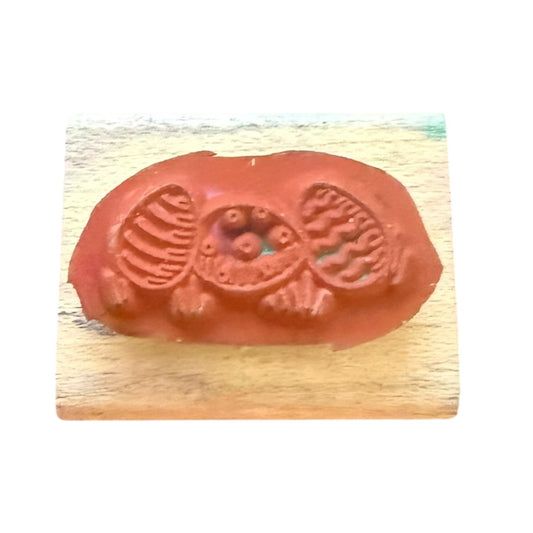 A terracotta-colored rubber stamp with a detailed Easter design, mounted on a light-colored wooden block against a white background.
