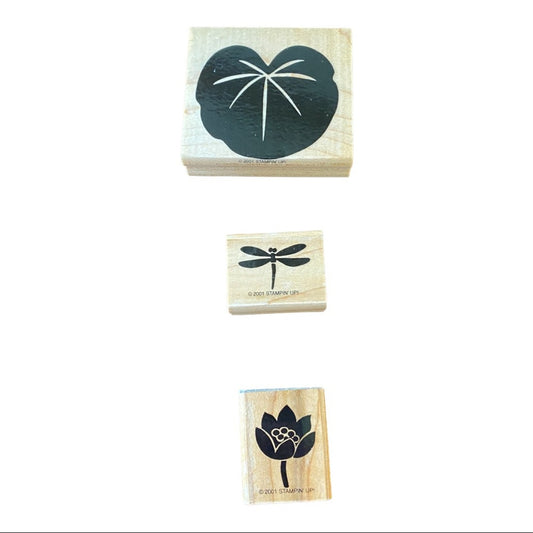 Three wooden rubber stamps shown vertically on a white background, featuring a lily pad, a dragonfly, and a lotus flower with small white details.