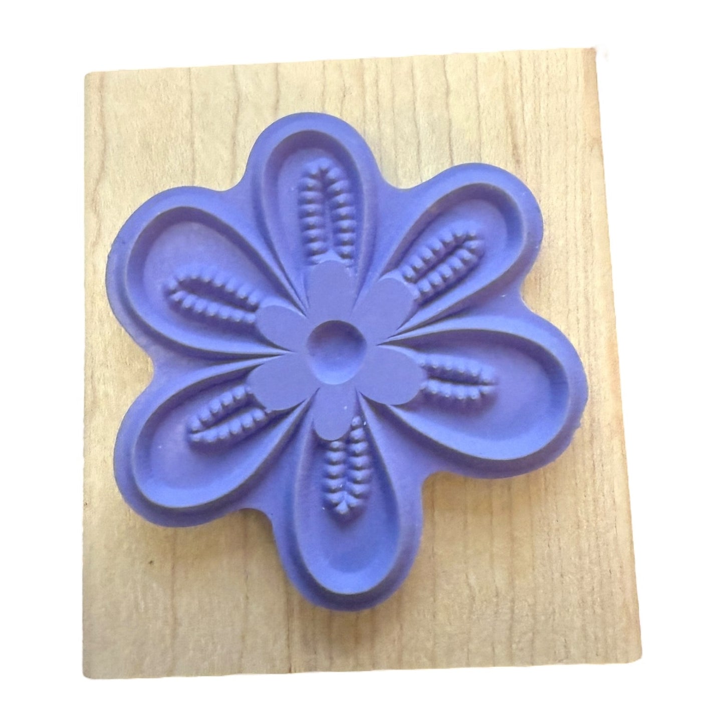 A purple flower-shaped stamp base mounted on a square light wood block, photographed against a plain white background.