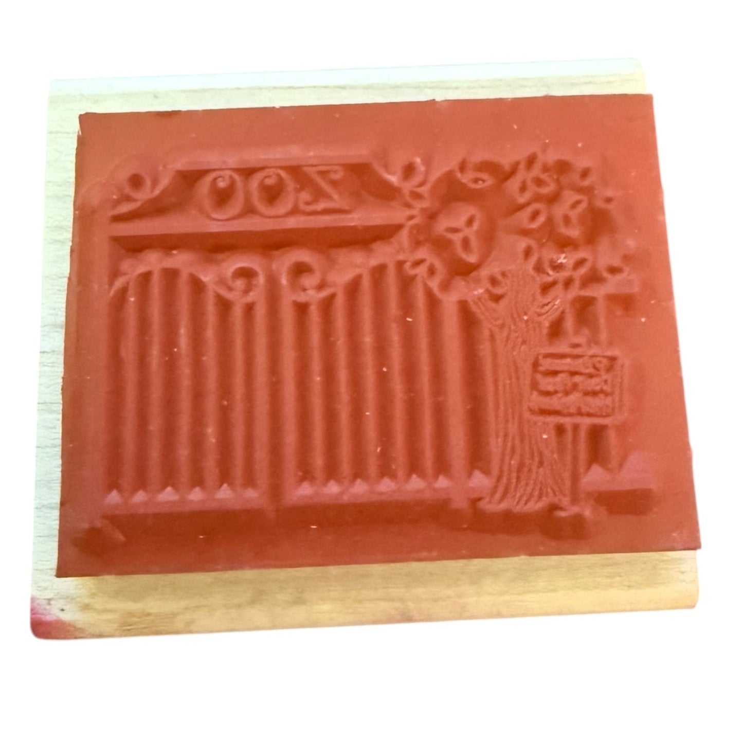 A red rubber stamp with a zoo design and mounted on a light-colored wooden block against a white background.