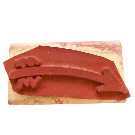 Red rubber stamp with an arrow design on a wooden block against a white background