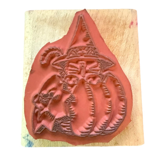Decorative stamp with a witch on a pumpkin design on a wooden block.