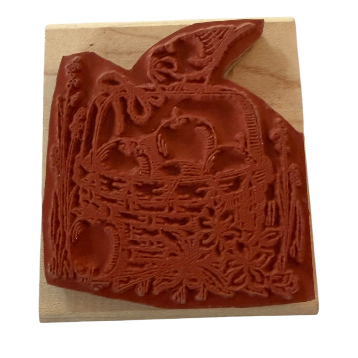 A wooden rubber stamp featuring an embossed autumn harvest design with apple, a basket, and a bird, shown on a light wood block against a white background.