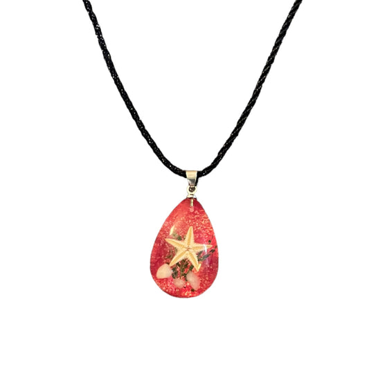 A teardrop-shaped pendant necklace featuring a red glittery resin body with a starfish and small seashell details, suspended on a black cord.