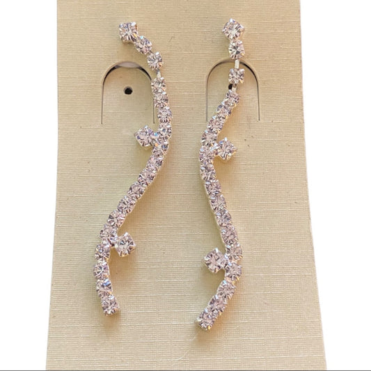 A pair of silver-tone wavy drop earrings set with clear rhinestones, displayed on a beige textured jewelry card.