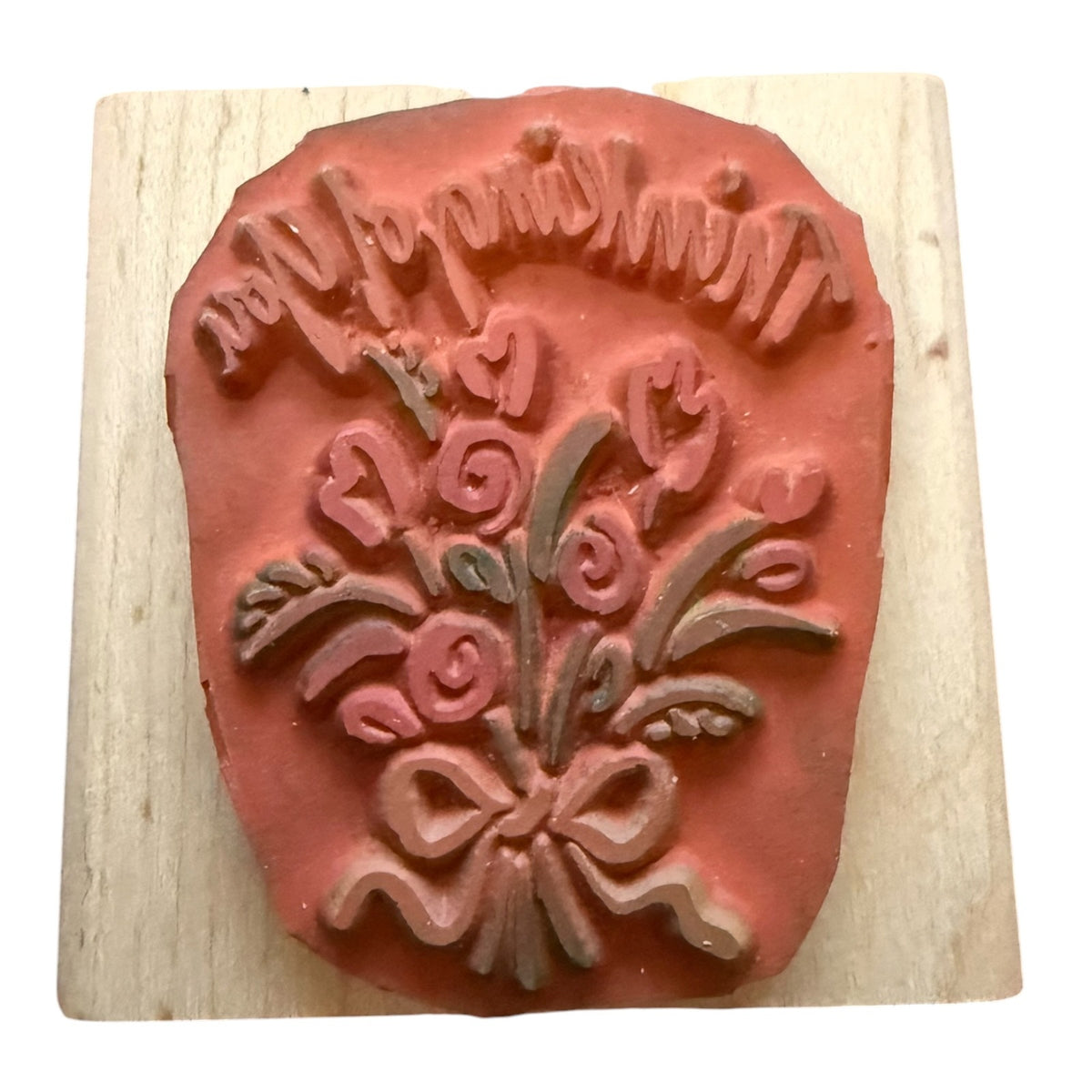 A terracotta-colored rubber stamp with a floral bouquet and bow design, mounted on a square light wood block against a white background.