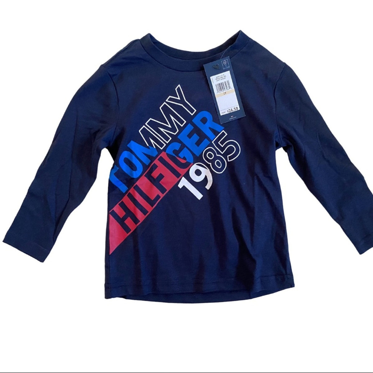 A navy blue long-sleeve Tommy Hilfiger graphic t-shirt with a diagonal red, white, and blue logo print on the front, complete with a retail hangtag.