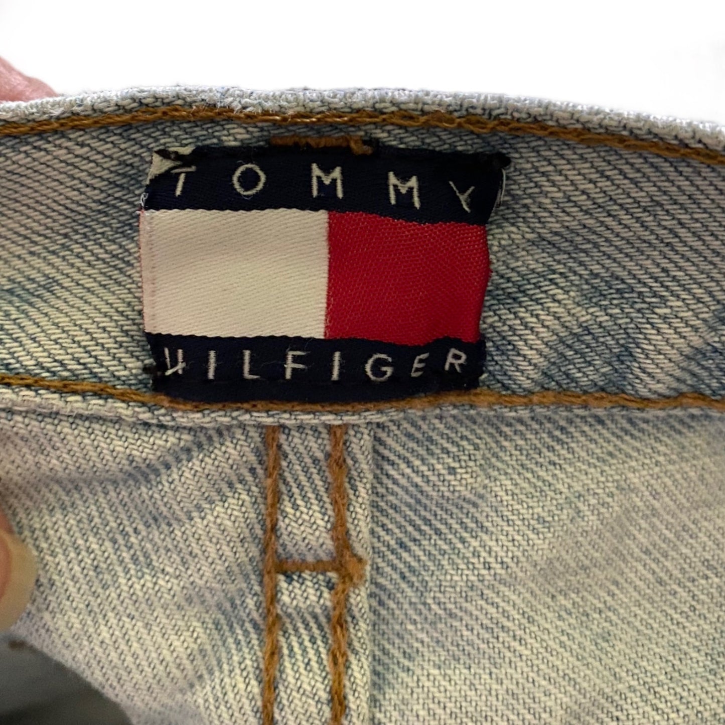Close-up of a denim jeans inner waistband showing the embroidered Tommy Hilfiger flag logo patch.
