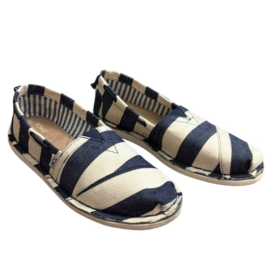 A pair of canvas slip-on shoes with navy blue and offw hite diagonal stripes, featuring a small white geometric logo on the toe and a striped fabric lining.