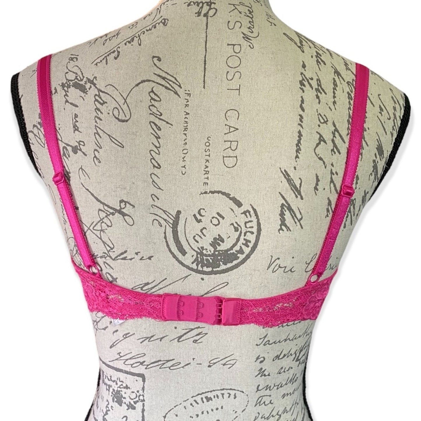 A bright pink lace bra with thin adjustable straps, displayed on a vintage-style fabric mannequin torso against a white background.