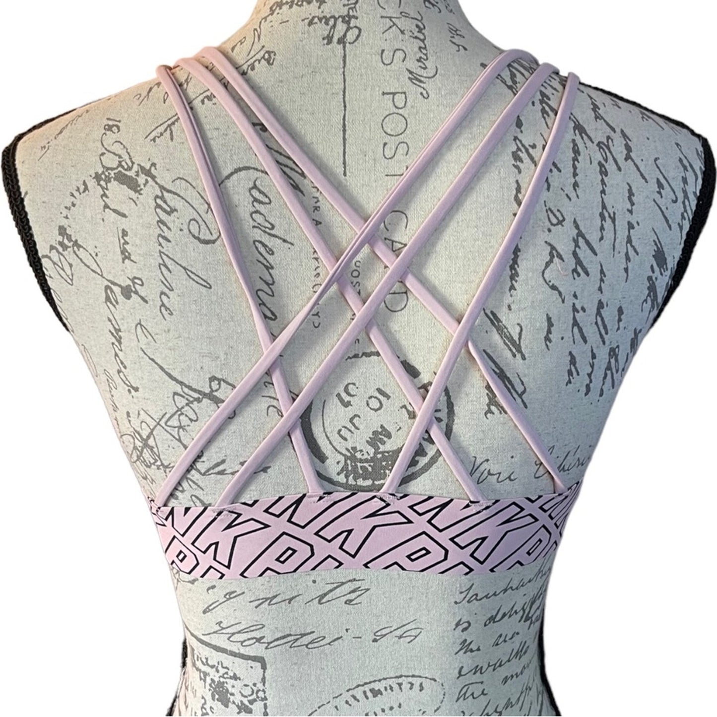 Pink bra with PINK written on it with criss-cross straps on a white background