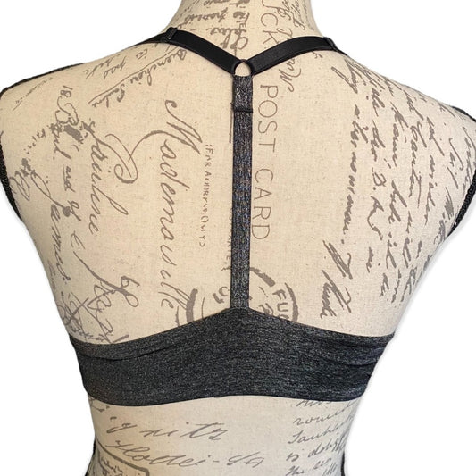 Back view of a dark gray bra displayed on a beige fabric mannequin torso with vintage script print, showing a wide underband and crossover shoulder straps.