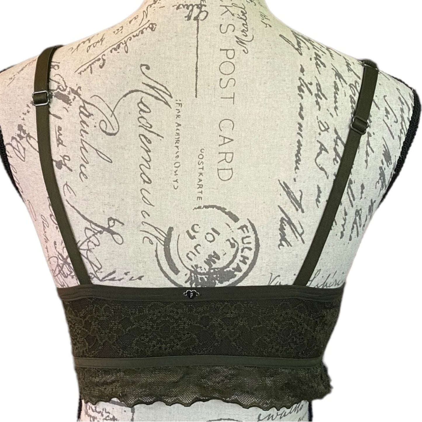 An green lace bralette displayed on a vintage-style printed dress form mannequin, showing the back view with shoulder straps and a lace underband.