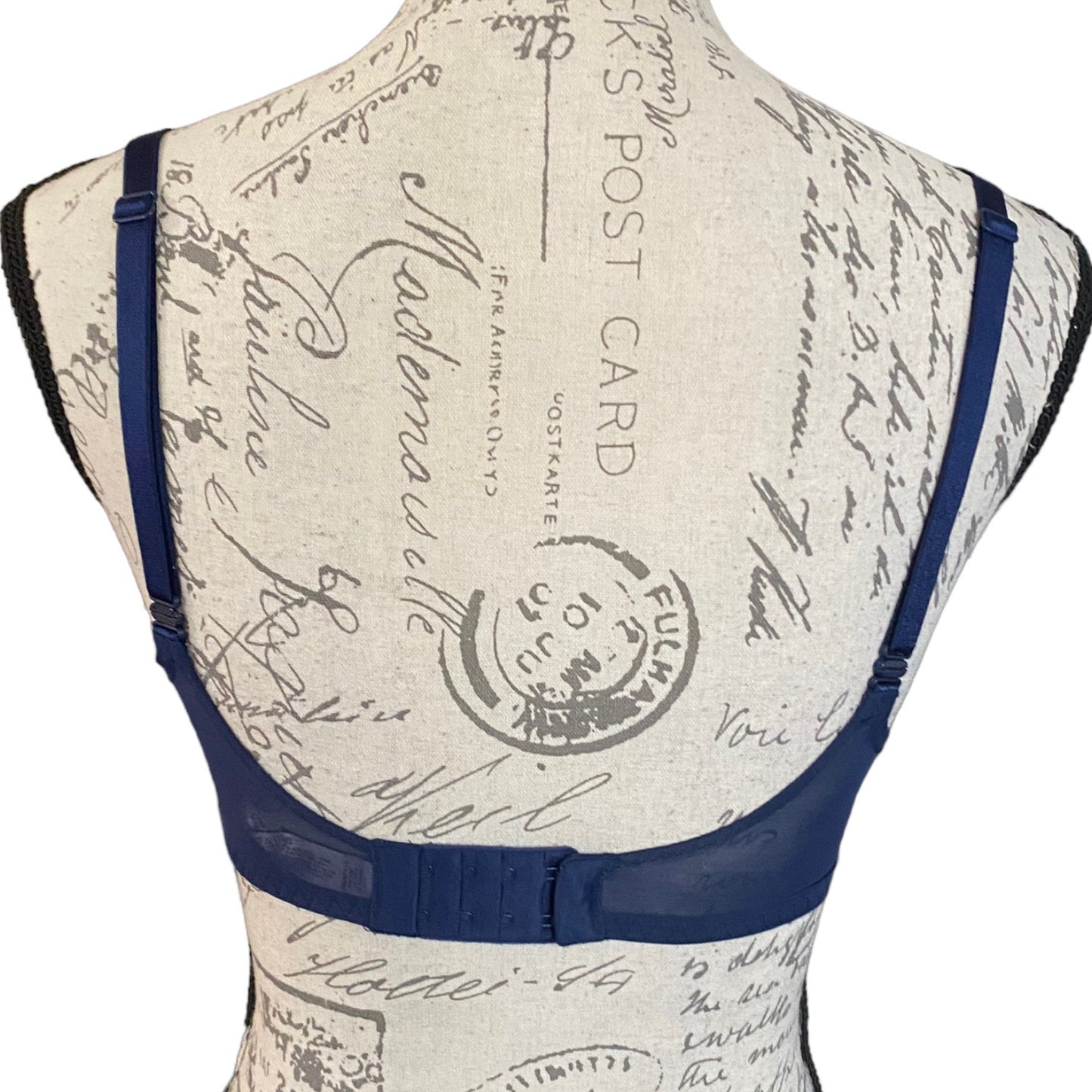 A navy blue bra with adjustable shoulder straps and a wide underband, displayed on a vintage-style patterned dress form mannequin against a white background.