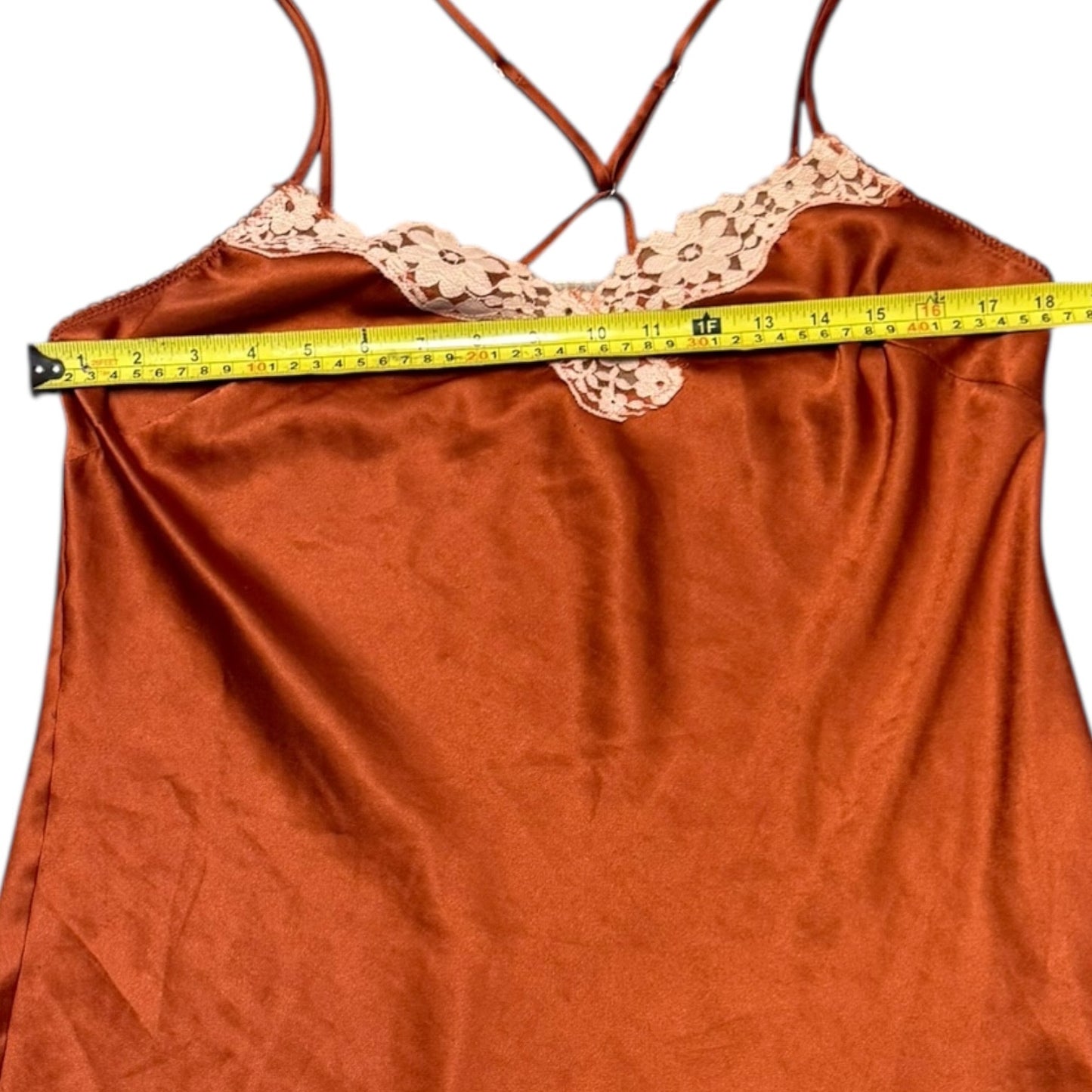 Orange satin slip dress with lace trim and a measuring tape draped over it on a white background