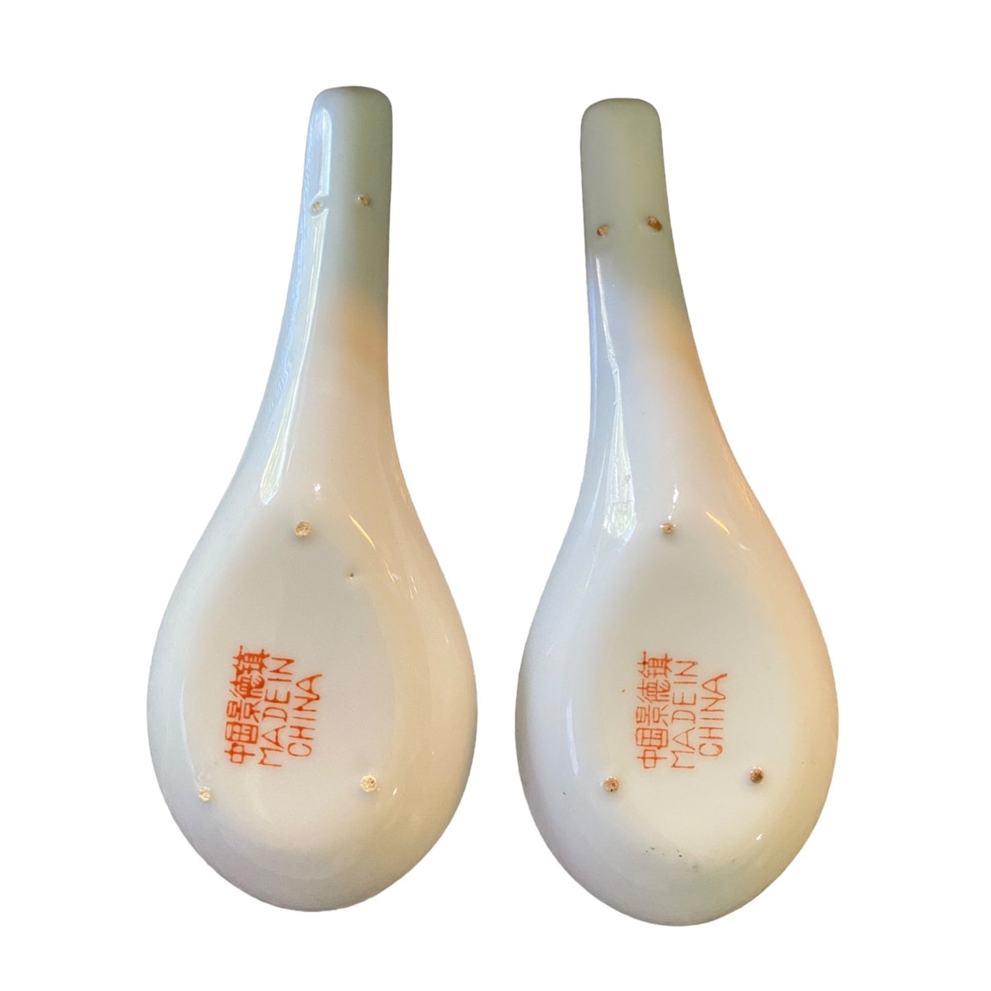 A pair of glossy white teardrop-shaped spoons with orange Chinese characters and 'MADE IN CHINA' printed on the bottom, set against a plain white background.