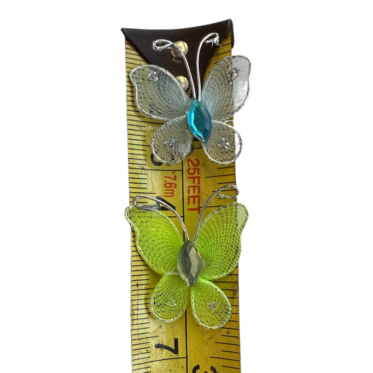Two butterfly-shaped embellishments shown on a yellow measuring tape against a white background. 