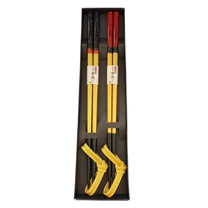 Set of yellow chopsticks with black and red accents in a black box on a white background