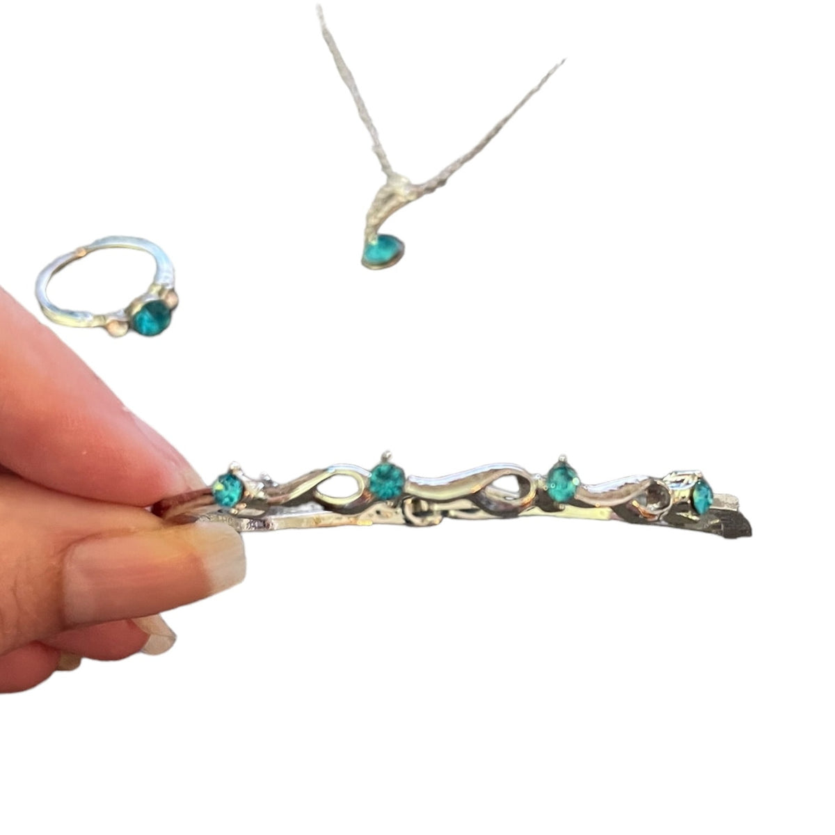 Hand holding a silver bracelet with turquoise stones, ring, and necklace on a white background