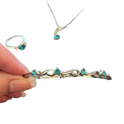 Hand holding a silver bracelet with turquoise stones, ring, and necklace on a white background