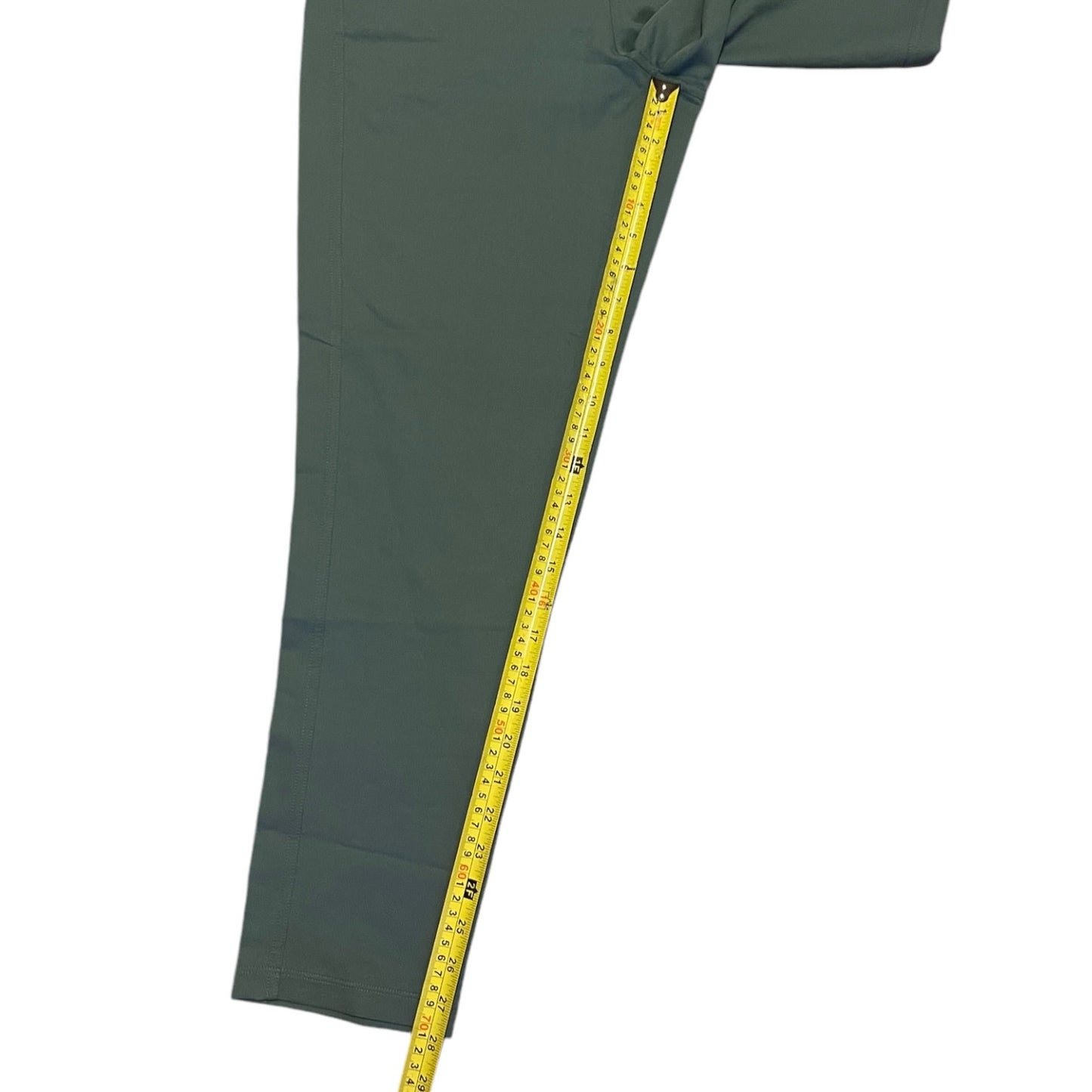 A close-up of a green pants with a yellow measuring tape running vertically along the side to show the length, on a plain white background.