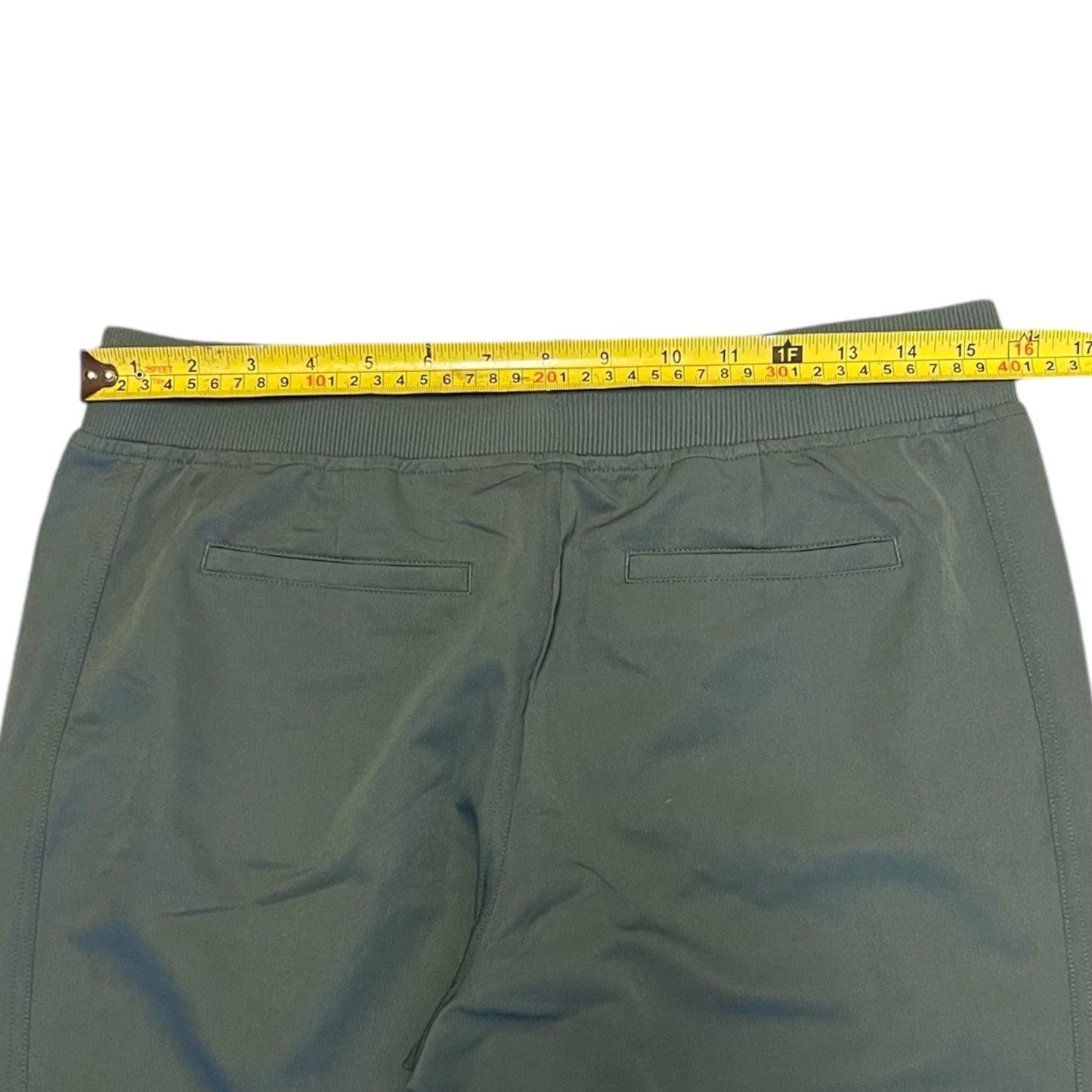 A pair of green pants shown from the back with a yellow tape measure stretched across the waistband to indicate the size.