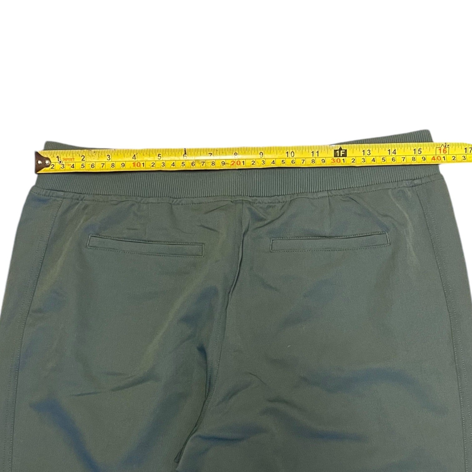 A pair of green pants shown from the back with a yellow tape measure stretched across the waistband to indicate the size.