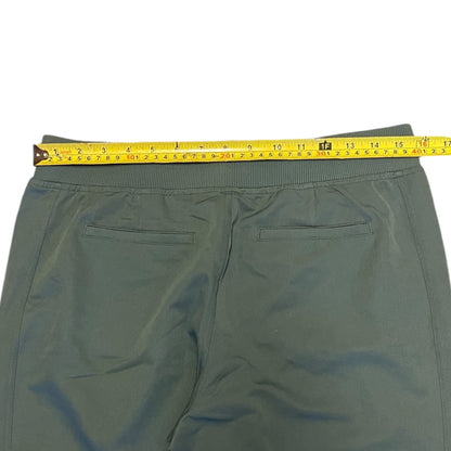 A pair of green pants shown from the back with a yellow tape measure stretched across the waistband to indicate the size.