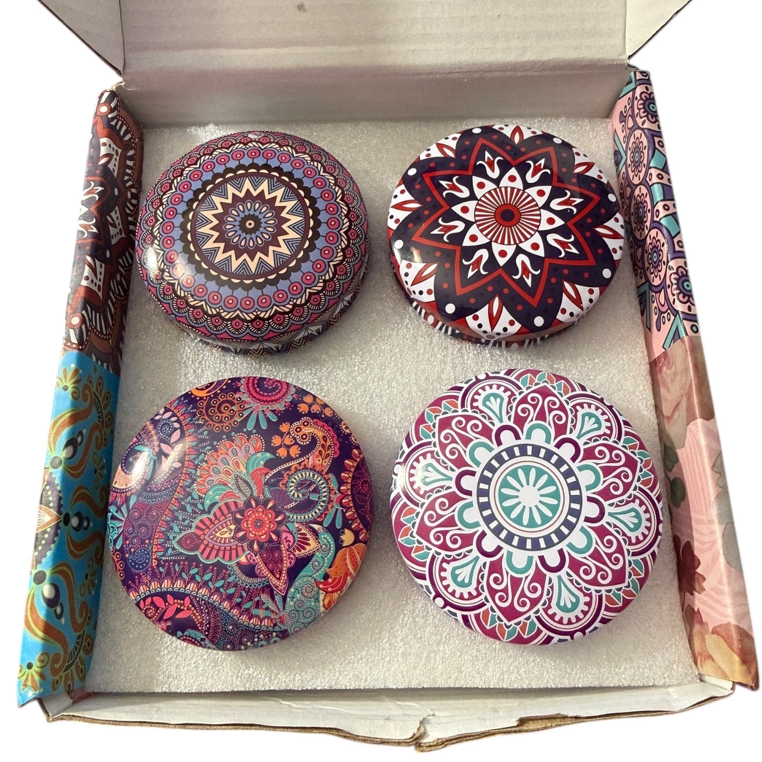 Four colorful mandala-patterned candles in a box with decorative paper.