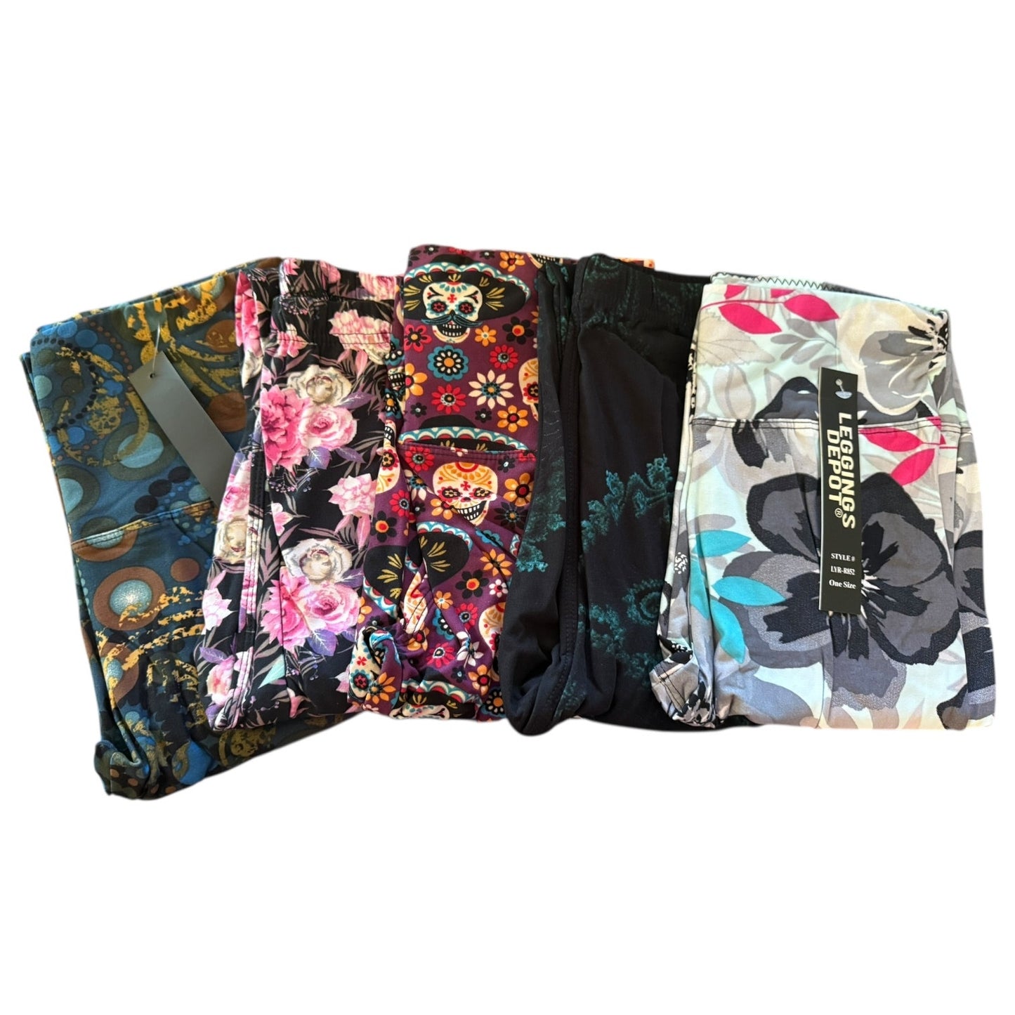 Five pairs of folded leggings in different colorful patterns, including floral, sugar skull, and abstract prints, displayed side-by-side on a white background.