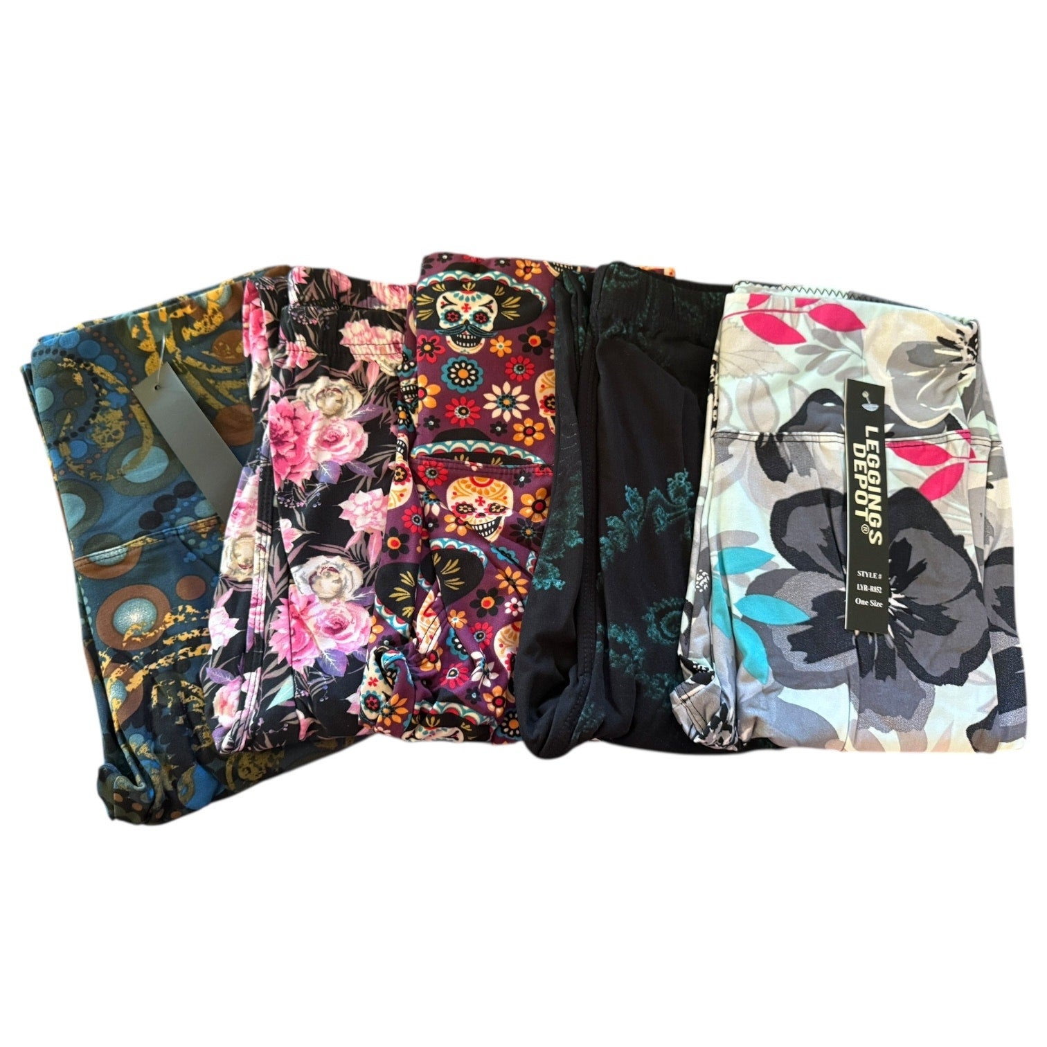 Five pairs of folded leggings in different colorful patterns, including floral, sugar skull, and abstract prints, displayed side-by-side on a white background.