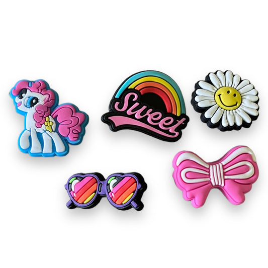 Set of colorful shoe charms including a pony, rainbow, daisy, and bow design on a white background.