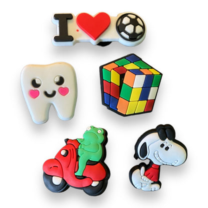 Five colorful vroc charms plain white background: a 'I' and heart with a soccer ball, a smiling tooth with pink cheeks, a multicolor Rubik's cube, a red scooter with a green frog, and a cartoon dog character in a red shirt.