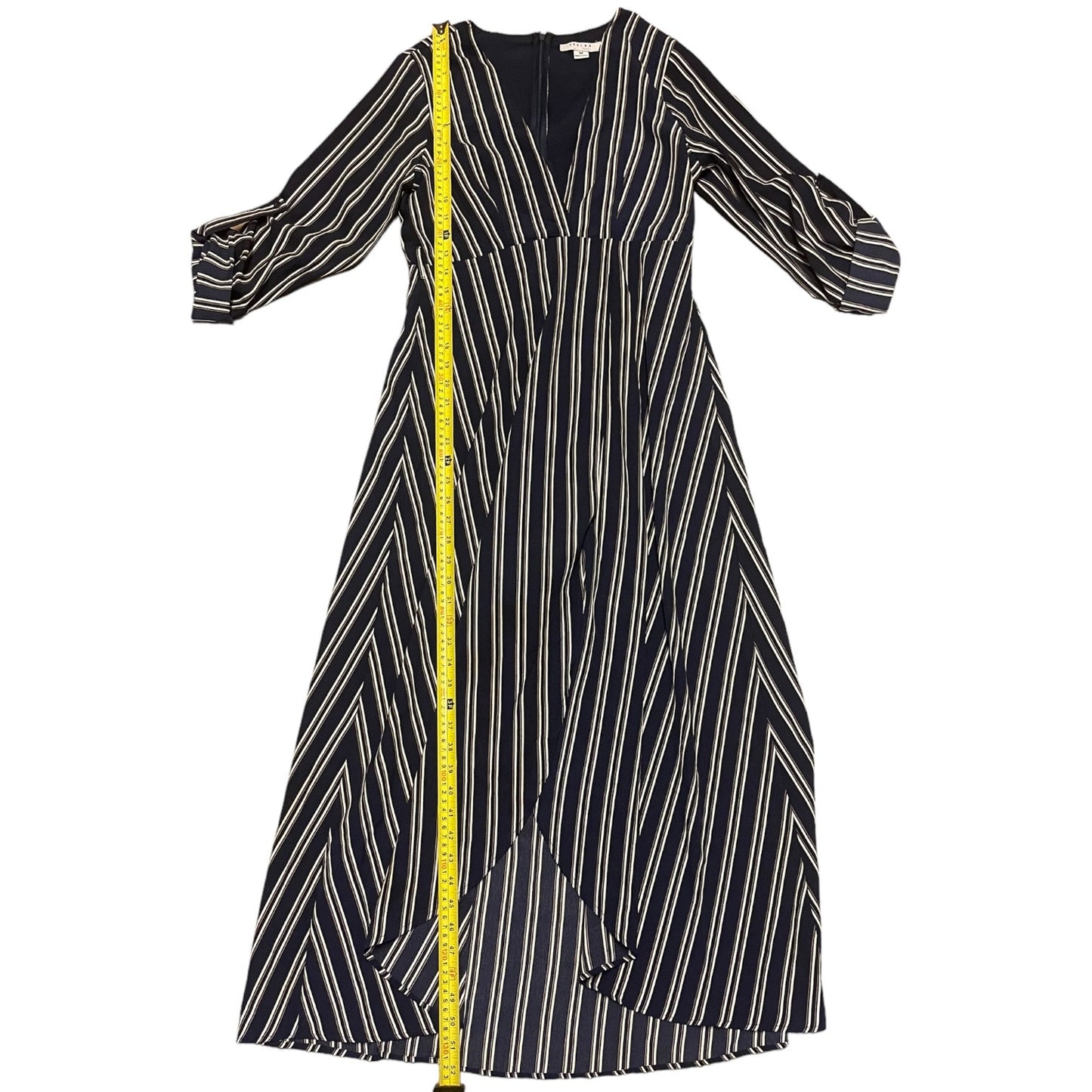 A blue midi dress with vertical white stripes and a yellow measuring tape draped down the front, shown against a plain white background.