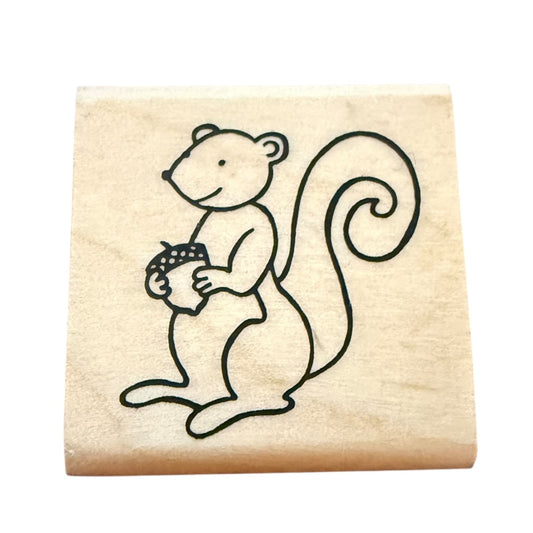 Wooden stamp with a cartoon squirrel holding an acorn on a beige background