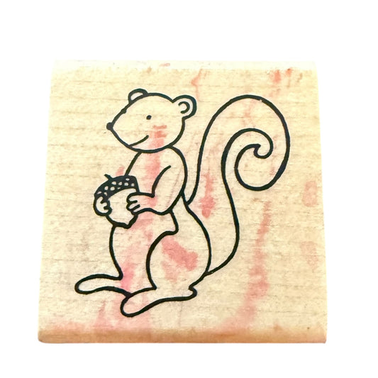 Rubber stamp with a cartoon squirrel holding an acorn on a pink and beige background