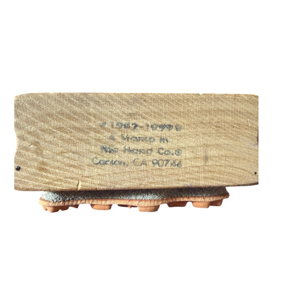 A vintage wooden stamp block with stamped text reading A Stamp In The Hand Co. San, CA 90722' resting on a white surface.