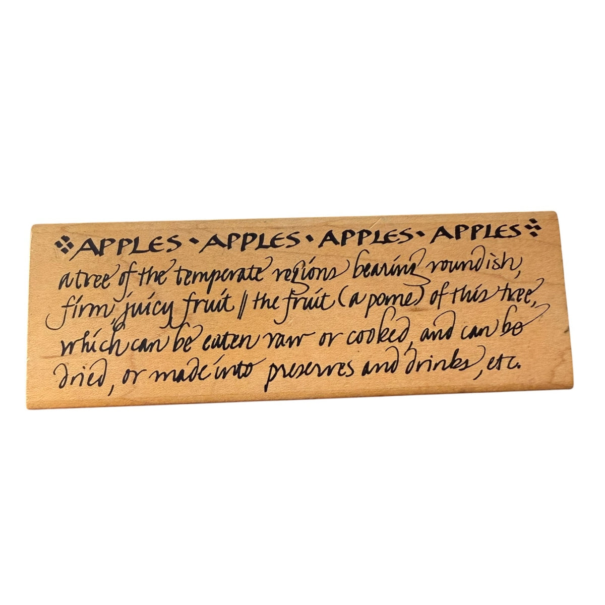 A rectangular wooden block with engraved black text defining 'Apples' on a plain white background.