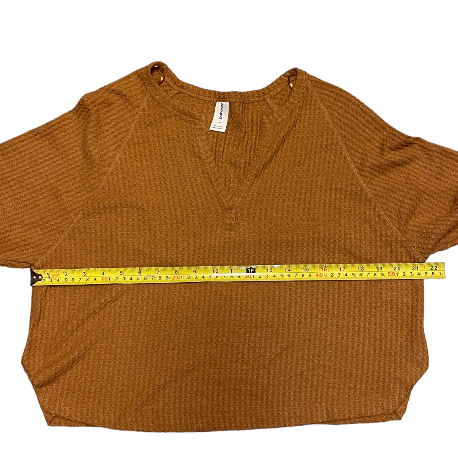 Brown textured shirt with a measuring tape laid across it on a white background
