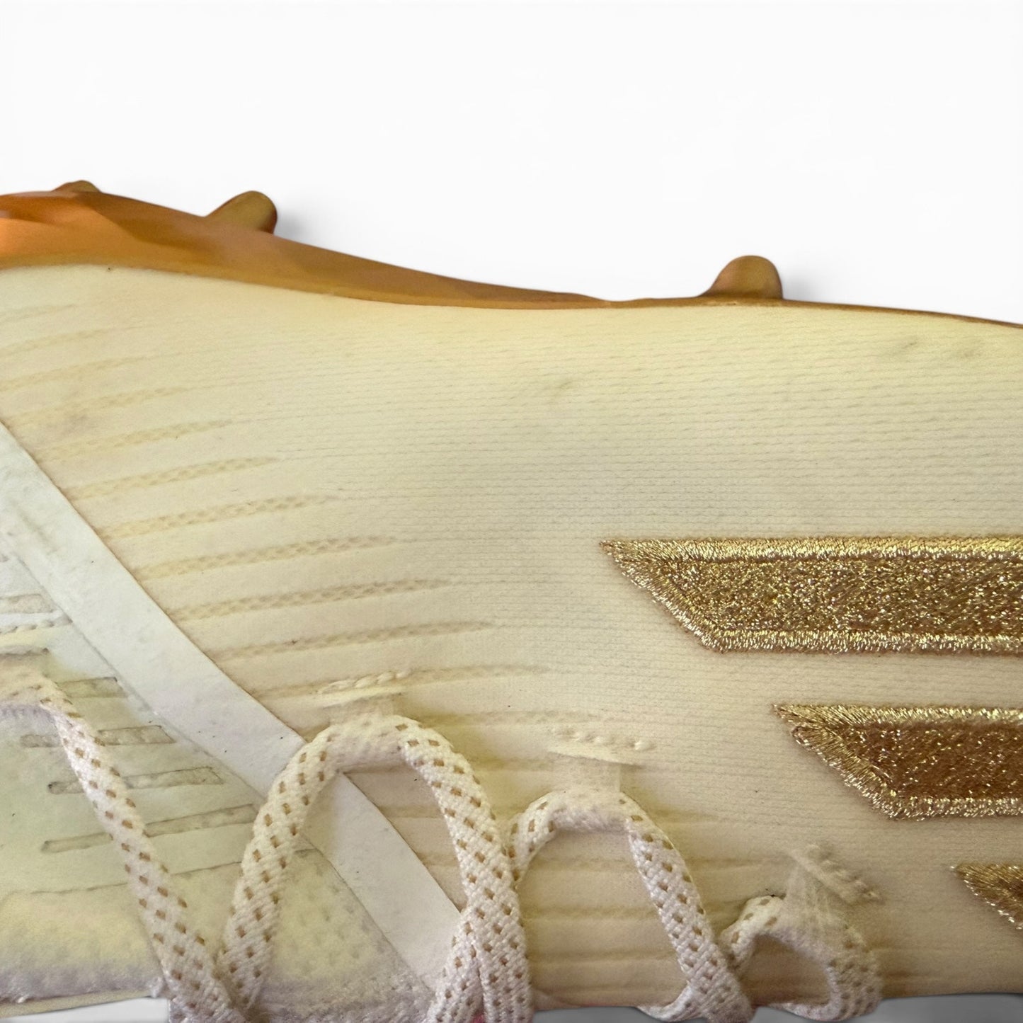 Close-up of a issue on shoes with a gold emblem and white lace trim on a white background