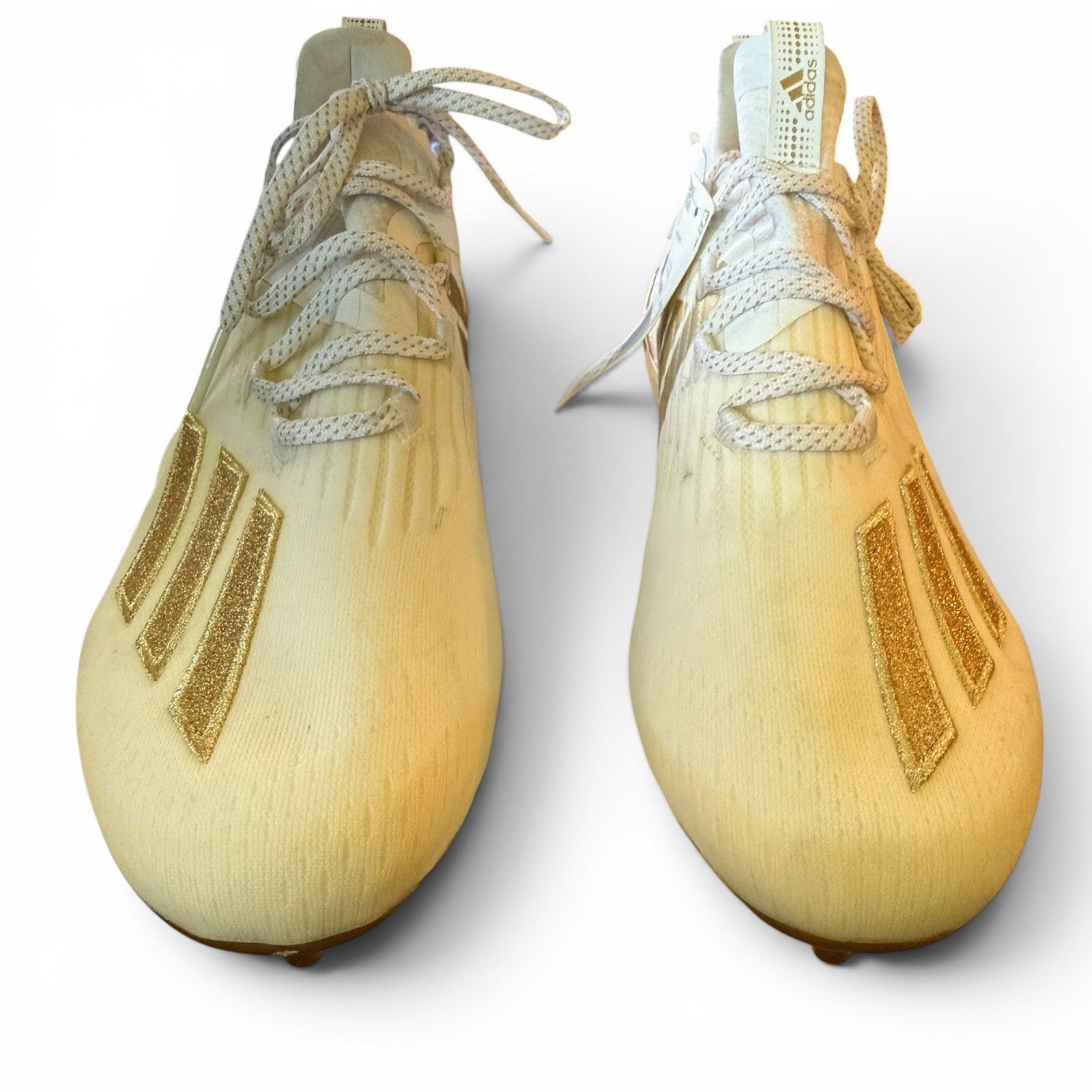 Pair of discolored soccer cleats with white laces on a light gray background