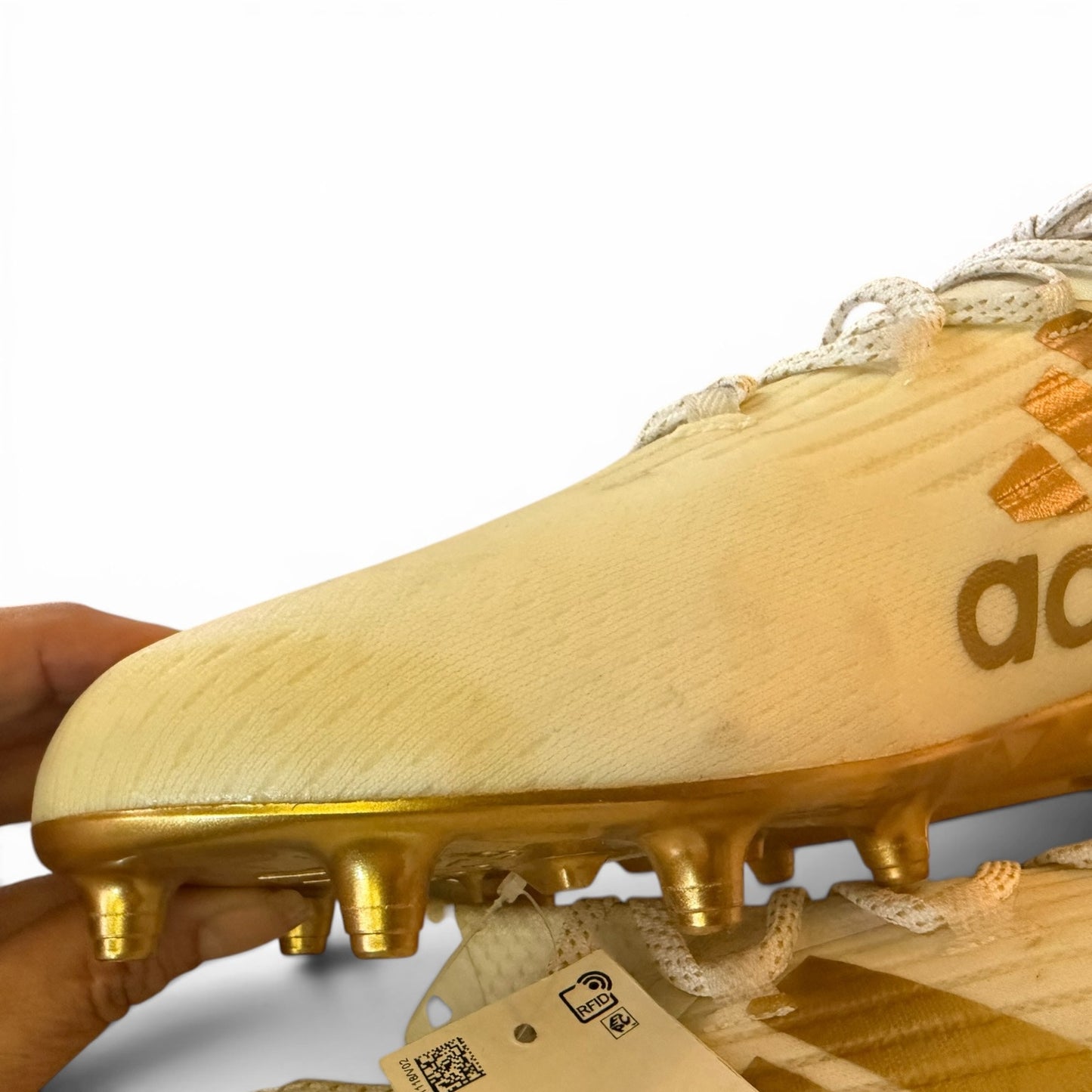 Discolored Gold soccer cleat with Adidas logo held by a hand on a white background