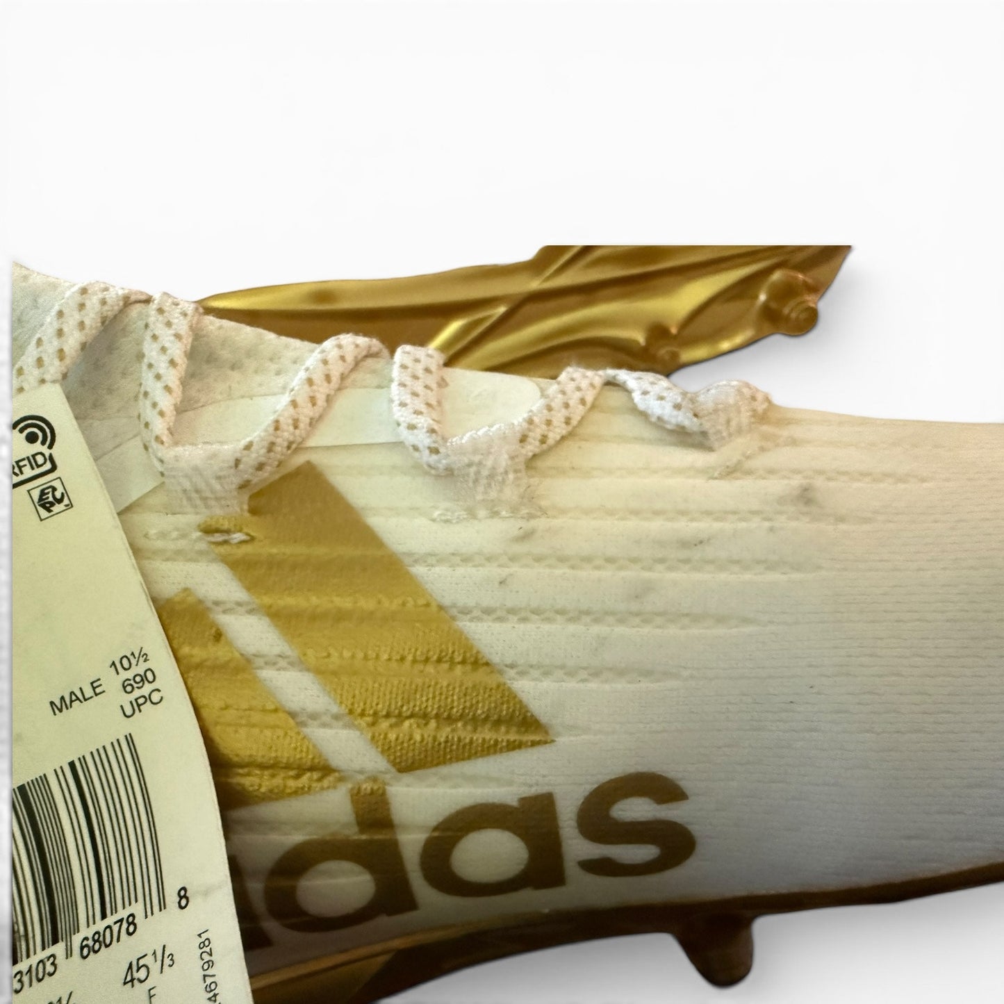 Close-up of a white sneaker with issues and gold accents and Adidas branding.