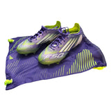 Front side of Purple and green soccer cleats on a matching purple bag with 'F50' branding.