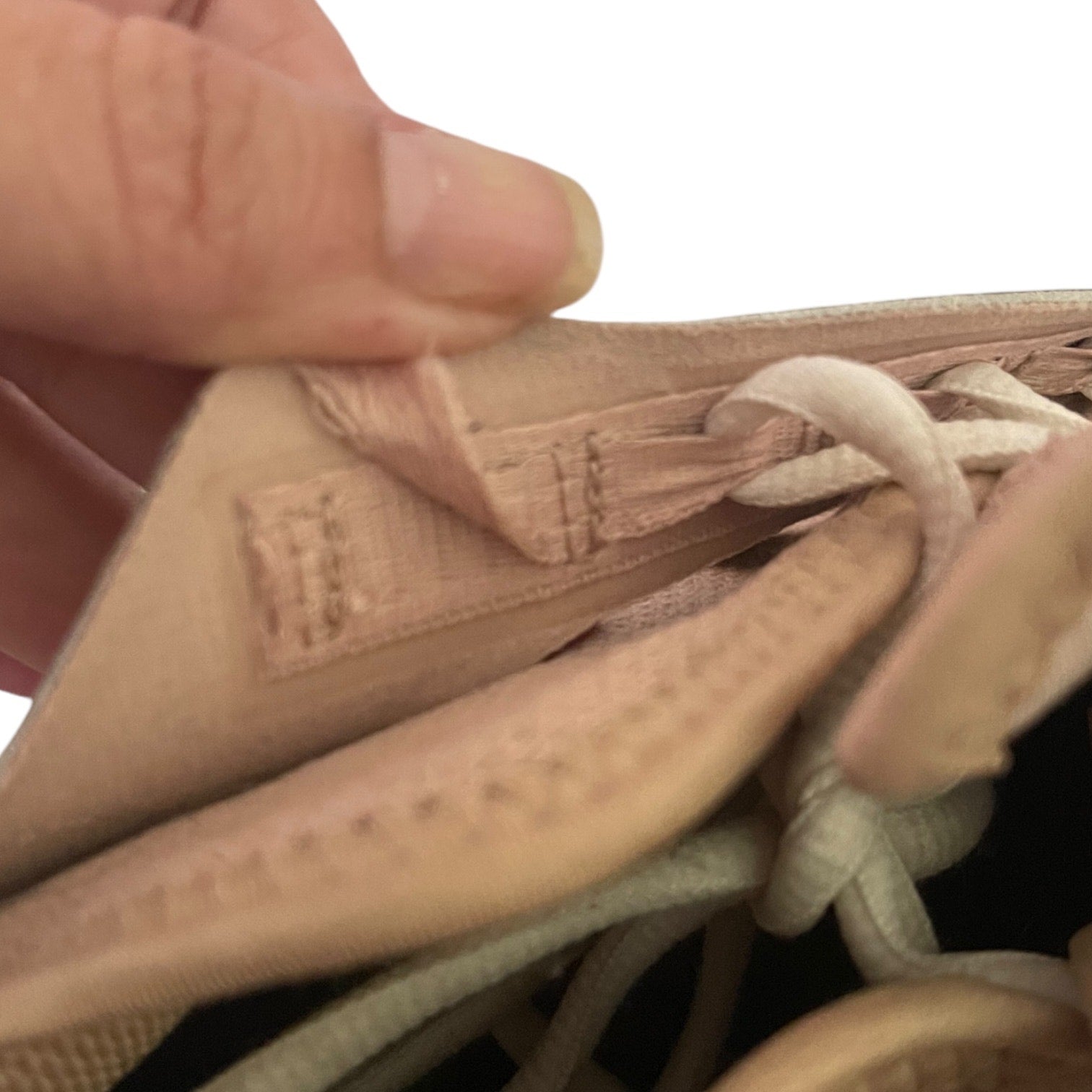 Issue on shoe with a brand label, held by a hand against a white background.