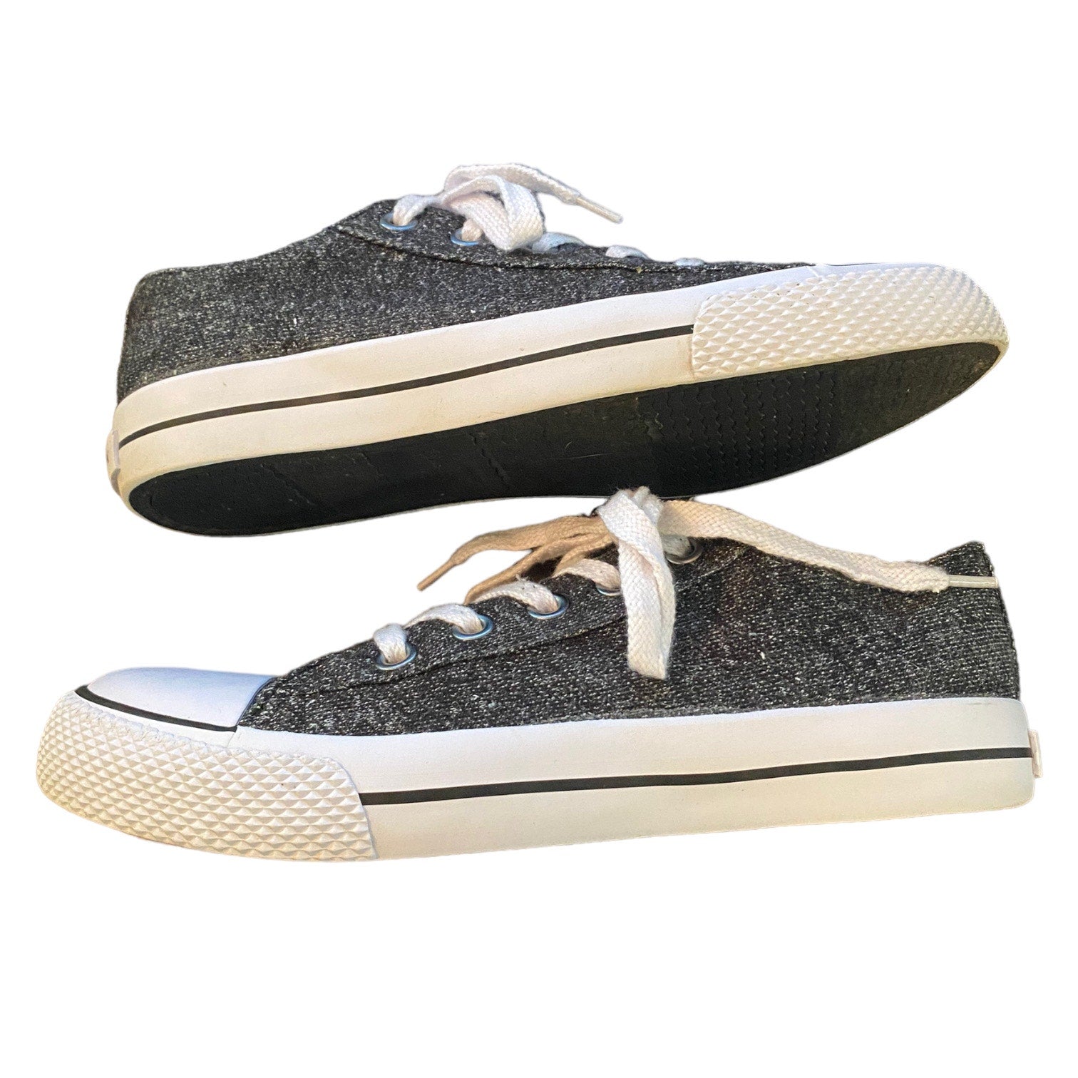 A pair of low-top canvas sneakers with a dark gray  upper, white laces, and off-white rubber soles, shown against a plain white background.