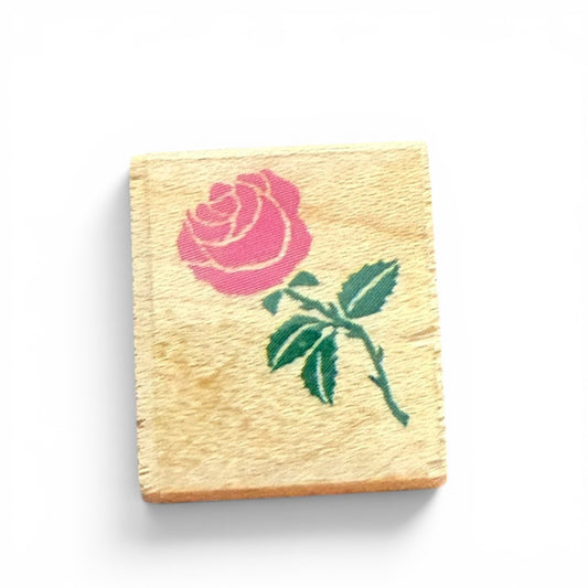 Wooden stamp block with a pink rose and green stem design on a white background