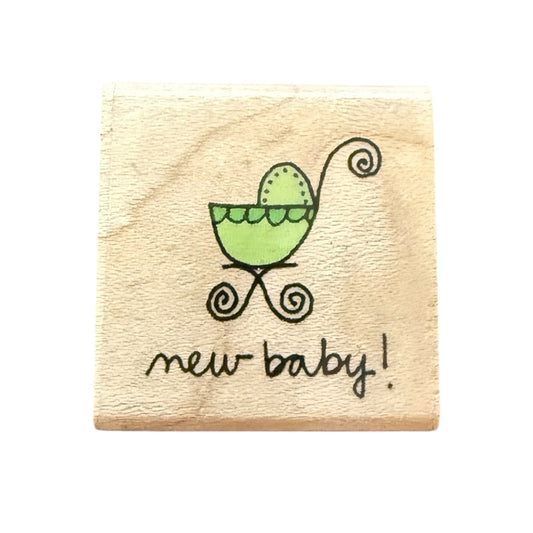 Wooden stamp with a green baby carriage and 'new baby!' text on a white background