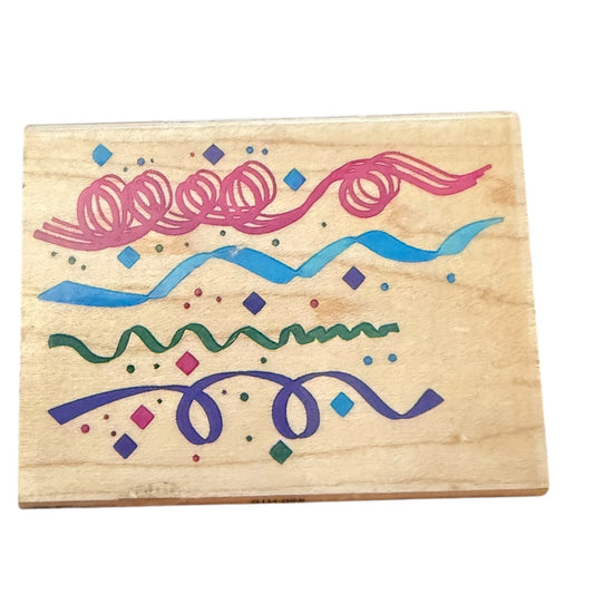 A square wooden stamp block featuring colorful printed wavy lines and dots in pink, blue, green, and purple on a light wood grain background.
