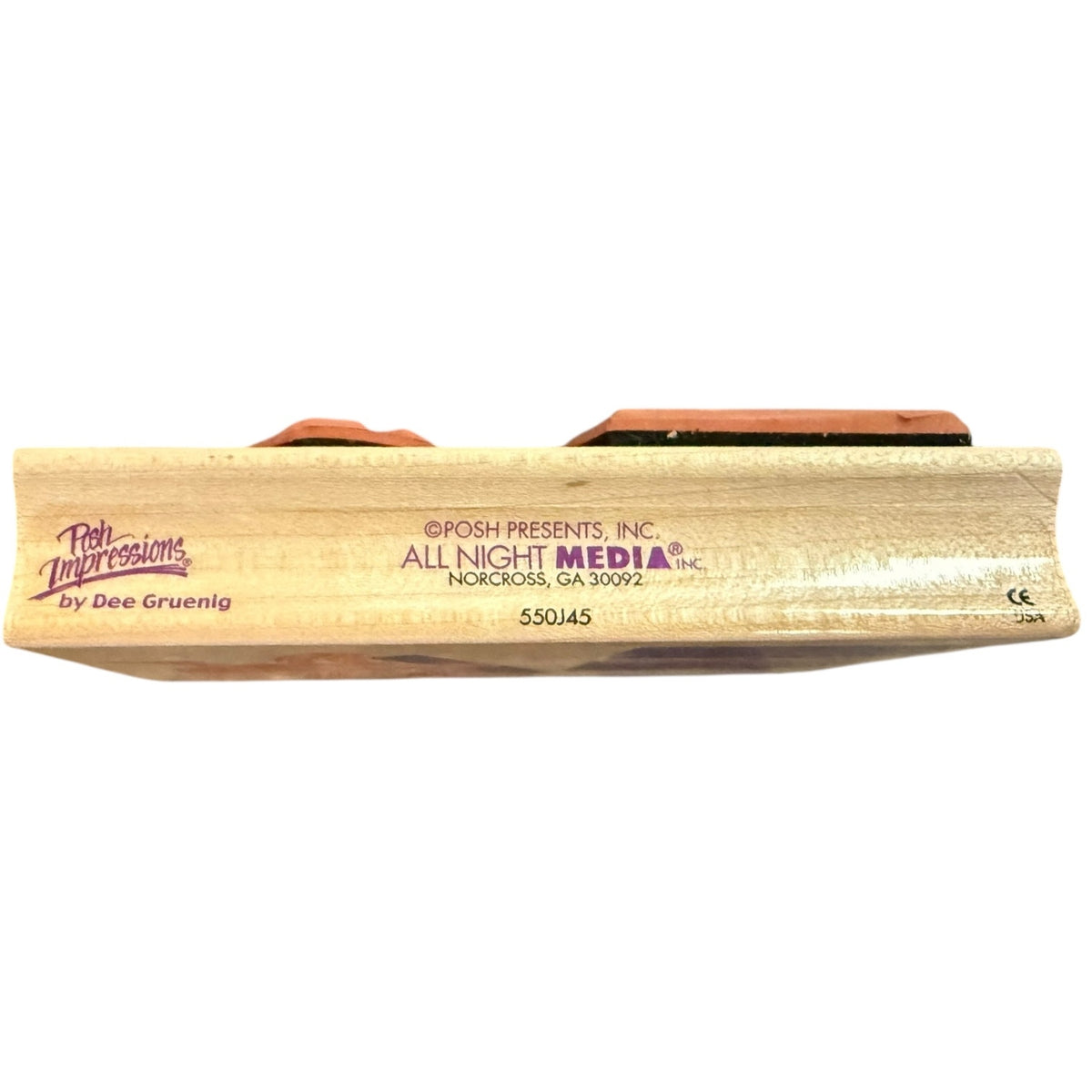 A close-up side view of a wooden stamp with printed branding and text, including 'Posh Impressions by Dee Gruenig' and 'All Night Media'.